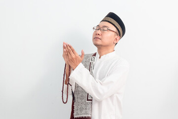 Asian Muslim man wearing white clothes doing praying hand pose during Ramadan Eid Al Fitr and eid...