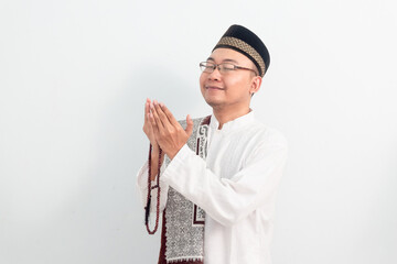 Asian Muslim man wearing white clothes doing praying hand pose during Ramadan Eid Al Fitr and eid...