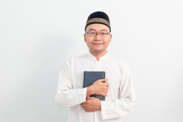 Asian Muslim man wearing white clothes holding quran during Ramadan Eid Al Fitr and eid adha days celebration isolated white background. Islamic celebration concept..