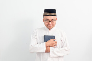 Asian Muslim man wearing white clothes holding quran during Ramadan Eid Al Fitr and eid adha days celebration isolated white background. Islamic celebration concept..