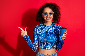 Smiling young woman in a stylish wavy-patterned top holding a cup, posing against a vibrant red background
