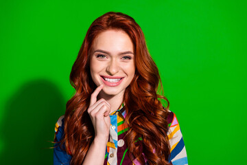 Smiling stylish young woman with red hair in colorful outfit against vibrant green background