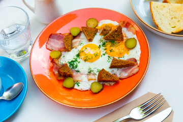 Fried eggs with bacon, croutons and pickles. Traditional Russian breakfast