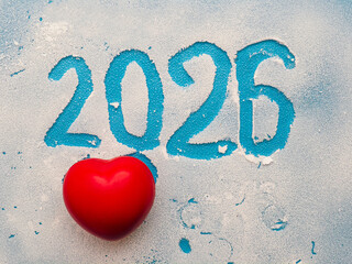 Glass with frost and hand written sign 2026 and read heart. Blue background. New Year celebration...