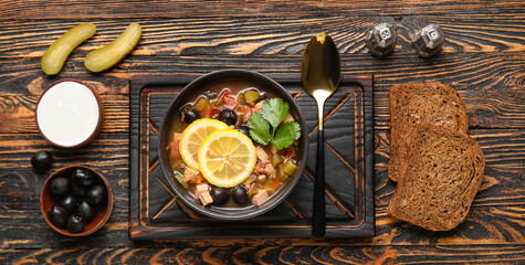 Bowl of tasty Hodgepodge soup with sour cream and bread on wooden background