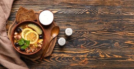 Bowl of tasty hodgepodge soup, spices, bread and sour cream on wooden background with space for text, top view