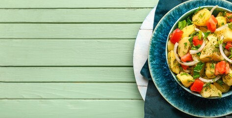 Plate of tasty potato salad on green wooden background with space for text, top view