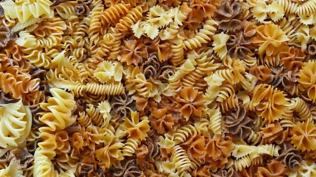 A background completely filled with different types of pasta, from fusilli to penne, packed tightly together to create a textured, golden surface.