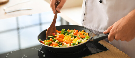 Male chef with spatula frying vegetables in kitchen, closeup