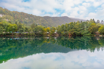 Fototapeta premium Quiet calm turquoise lake with trees in the background and mountains in the background with blue sky reflecting in the lake