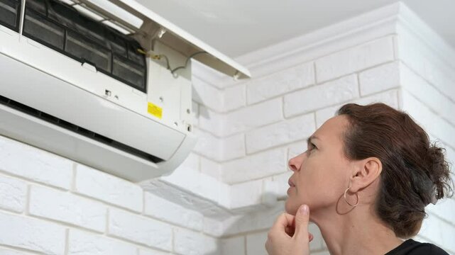 Woman by remote controller by conditioner. A woman look at the broken air conditioner with remote controller in the room.