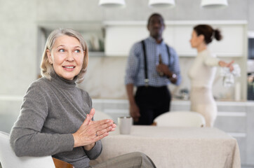 Elderly woman smiling during family quarrel between couple of adult man and woman in kitchen