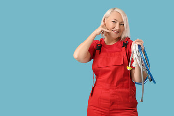 Mature female plumber with pipes showing CALL ME gesture on blue background
