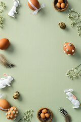 Happy Easter vertical banner design. Frame of brown Easter eggs decorated flowers, quail eggs, ceramic bunnies on pastel green background. Flat lay, top view, copy space.