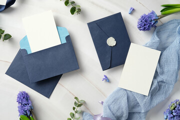 Elegant wedding stationery set with navy blue envelopes, blank cards, and hyacinth flowers on a marble background. Flat lay, top view.
