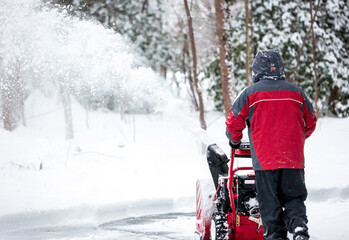 A person operating a snow blower to clear a driveway
