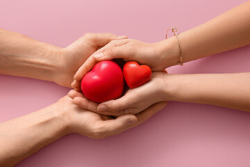 Couple holding hearts on pink background, top view