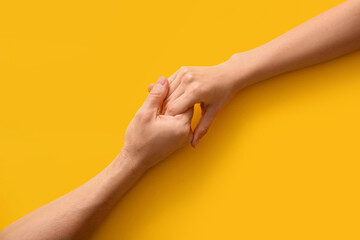 Couple holding hands on yellow background, top view
