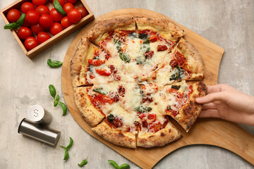 Hand taking slice of tasty pizza Margarita on grey grunge background
