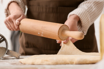 Woman rolling out fresh dough in kitchen