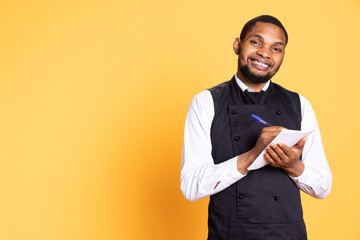 Skilled waiter with apron takes meal orders from clients on a notebook, writing down important...