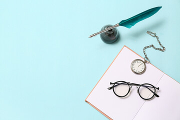 Open book with nib pen, inkwell, pocket watch and glasses on blue background