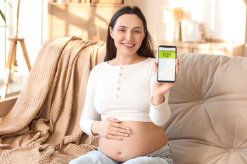 Young pregnant woman with mobile phone measuring blood sugar level on sofa at home. Gestational...
