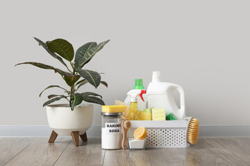 Flowerpot and basket with cleaning products on laminate floor against grey wall