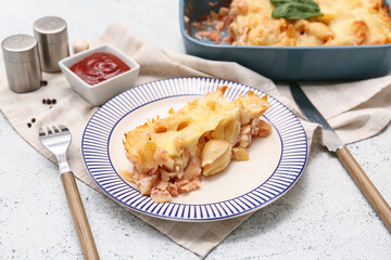 Plate with tasty baked pasta, cheese, bowl of ketchup and cutlery on light background