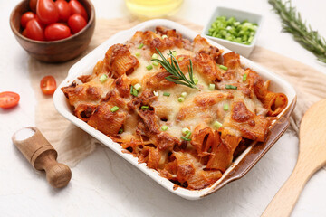 Baking dish with tasty pasta, rosemary, cut green onion and tomatoes on white background