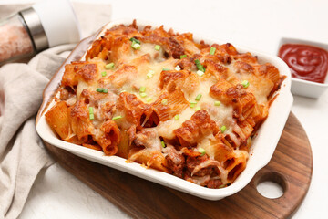 Baking dish with tasty pasta, cut green onion and cheese on white background
