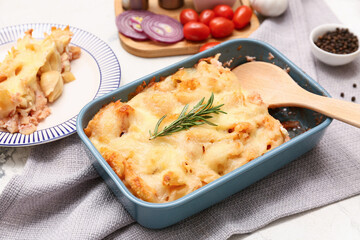 Baking dish with tasty pasta, rosemary and cheese on light background
