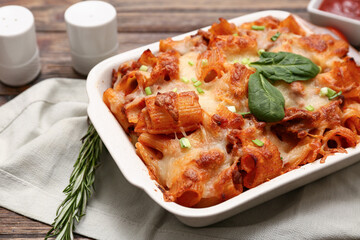 Baking dish with tasty pasta, cut green onion, spinach leaves and rosemary on wooden background