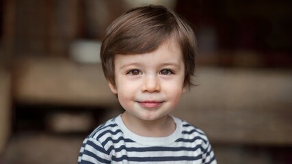 Little boy with a smile. He has dark brown hair and is wearing a striped shirt