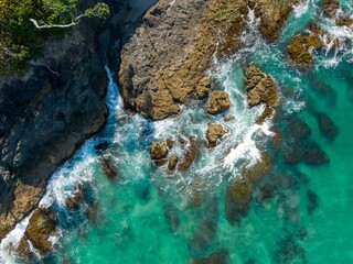 Coastal rocks and turquoise water. Waves crash against the rocky shore. Aerial view. Elliot Bay, Rawhiti, Northland, New Zealand