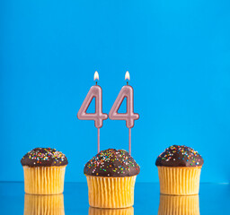Three birthday cupcakes with number 44 candle - Blue background.