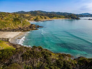 Naklejka premium Tranquil coastal scene. Waves gently lap a sandy beach, framed by lush greenery and rocky cliffs. A beautiful New Zealand coastline. Elliot Bay, Rawhiti, Northland, New Zealand