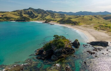 Stunning aerial view of a secluded Elliot Bay beach cove. Crystal-clear turquoise water laps the sandy shore, framed by lush green hills. Tranquil coastal scene.  Rawhiti, Northland, New Zealand
