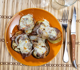 Piece of meat put on slice of eggplant and potato with cut onion and cheese baked in oven
