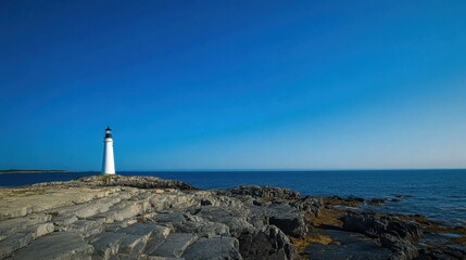 Obraz premium Serene coastal lighthouse standing tall on rocky shores against a deep blue sky.