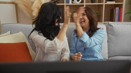 Women enjoying time together in a cozy living room, showcasing their happiness with laughter and high-fives, enveloped by warm interior decor creating a friendly atmosphere.
