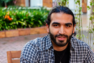 Colombian Latino adult male with rocker style, with boots and grunge shirt, looking at the camera. Man with beard and long hair