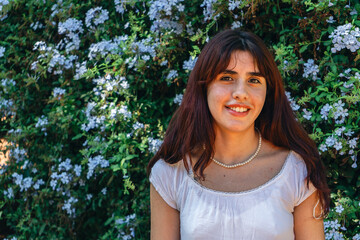 Fototapeta premium Young woman smiling in front of flowering bush with delicate pearl necklace