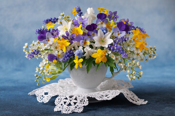 Bouquet of wild spring flowers in a cup, blue muscari, hepatica, pansies, yellow anemones, white bird cherry. Beautiful card