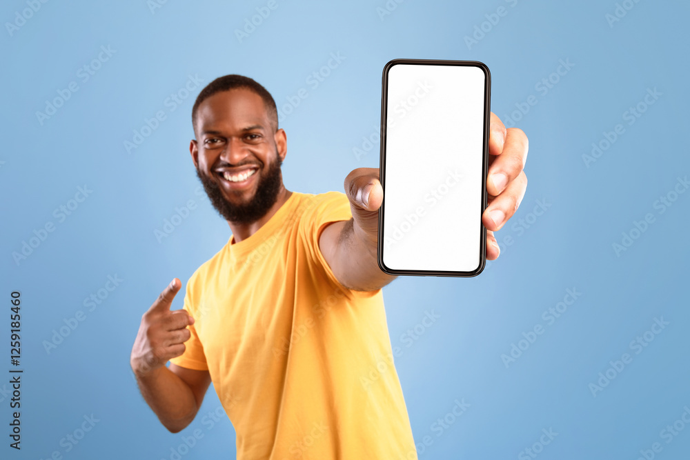 Poster excited african american guy in casual wear pointing at cellphone with empty screen on blue studio b