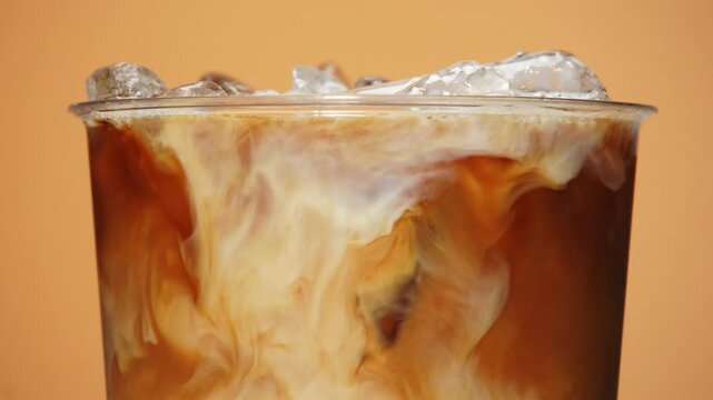 Close-up of iced coffee as creamy milk swirls through the dark liquid.