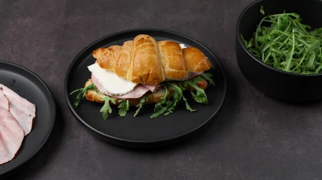 Croissant sandwich with black forest ham, panela cheese and arugula leaves on a black plate
