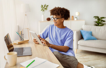 Web based schooling. Positive black teenager using tablet pc and laptop for online education at home. Cheerful African American adolescent taking part in webinar, talking to teacher on web