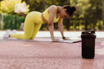 Sports Nutrition. Selective focus on black shaker on basketball field ground. Young black woman...