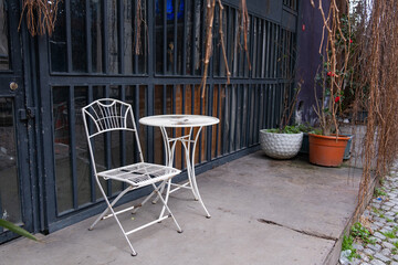 Solitary white metal table and chair set against a minimalist industrial building. Outdoor seating area with a white metal table and chair, situated in front of a grimy industrial building